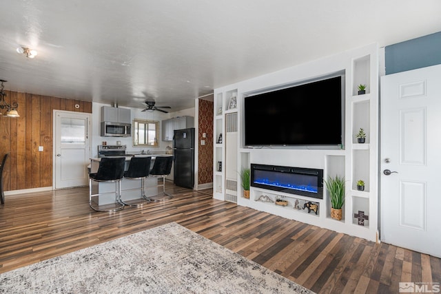 living room featuring a ceiling fan, a glass covered fireplace, dark wood finished floors, and built in shelves