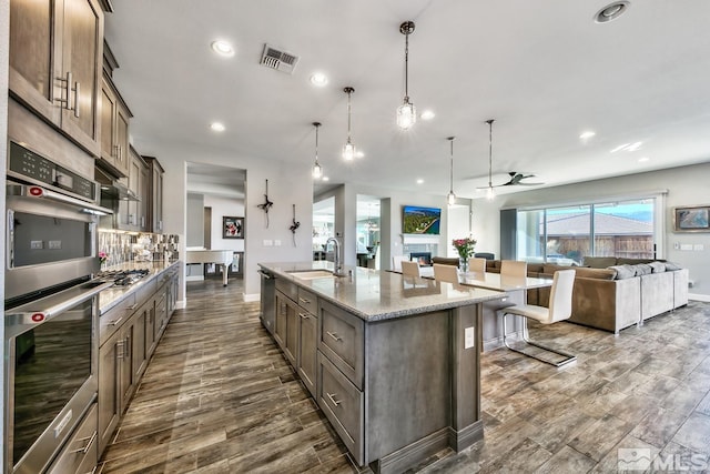kitchen with dark wood-style flooring, an island with sink, visible vents, a kitchen bar, and a sink