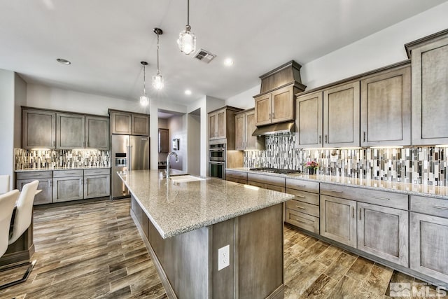 kitchen featuring under cabinet range hood, visible vents, decorative backsplash, stainless steel appliances, and a sink