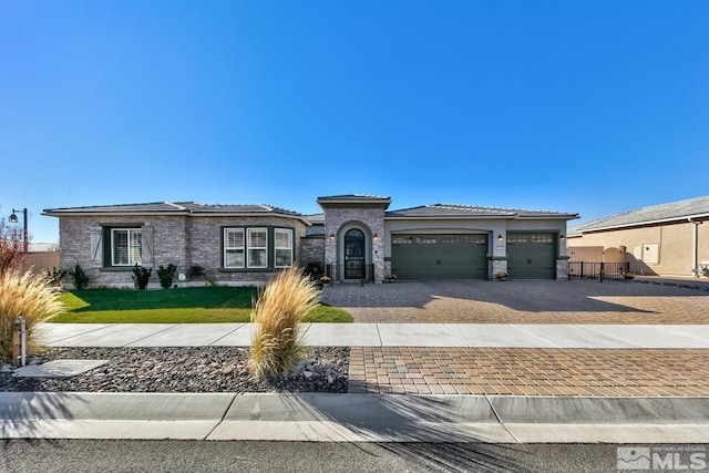 prairie-style home with stone siding, decorative driveway, an attached garage, a front yard, and a tiled roof