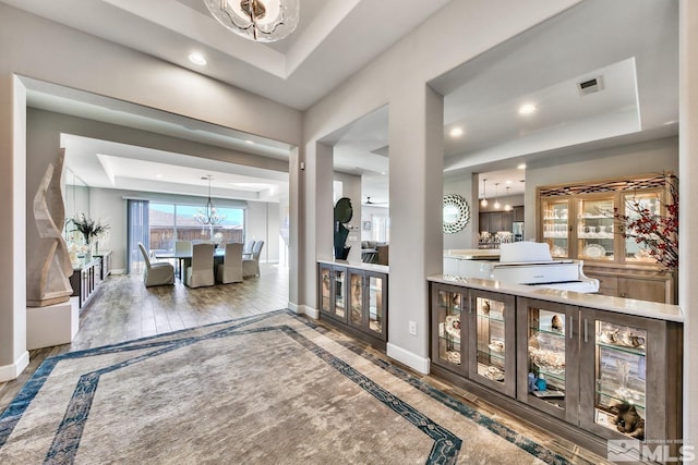 foyer entrance with baseboards, visible vents, a tray ceiling, and an inviting chandelier