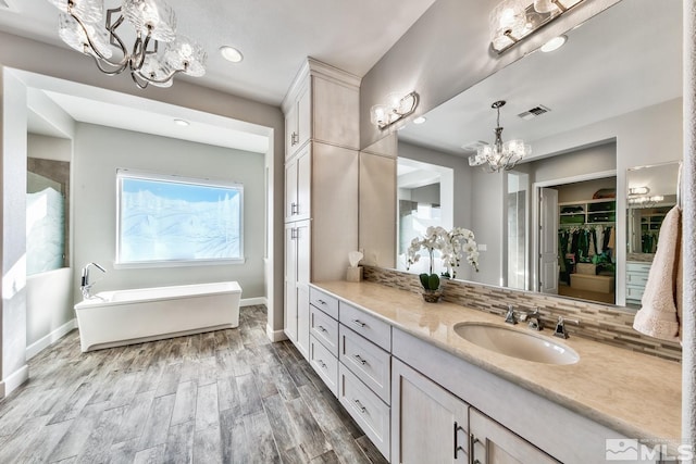 full bath featuring an inviting chandelier, a freestanding tub, vanity, visible vents, and backsplash