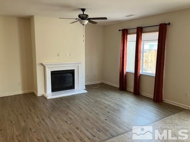 unfurnished living room featuring visible vents, baseboards, ceiling fan, wood finished floors, and a glass covered fireplace
