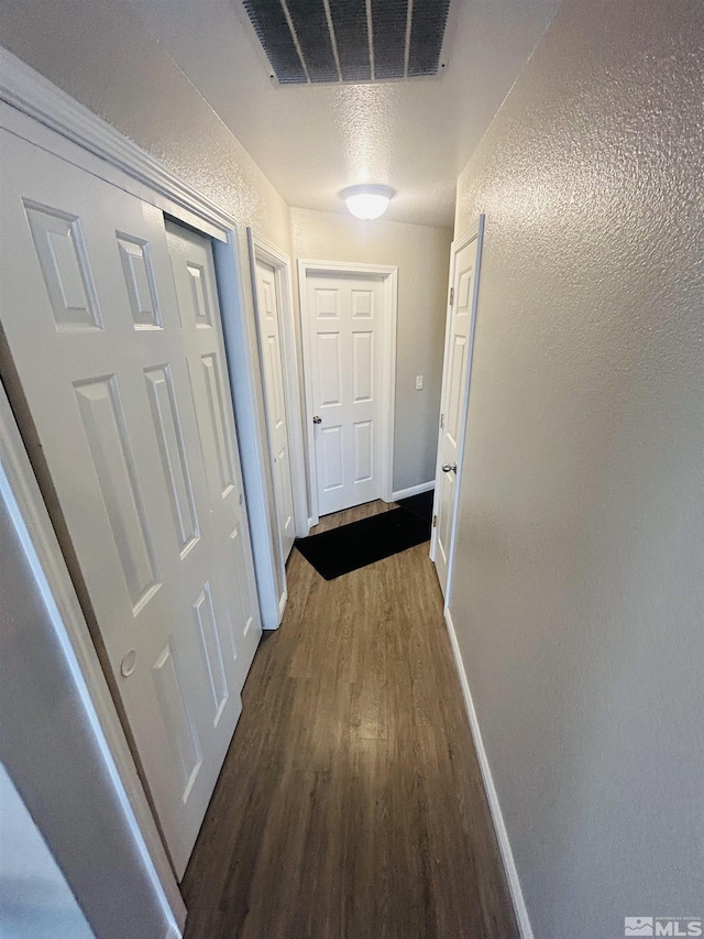 hall featuring visible vents, baseboards, and wood finished floors