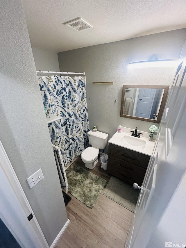 bathroom featuring a textured ceiling, vanity, visible vents, wood finished floors, and a textured wall