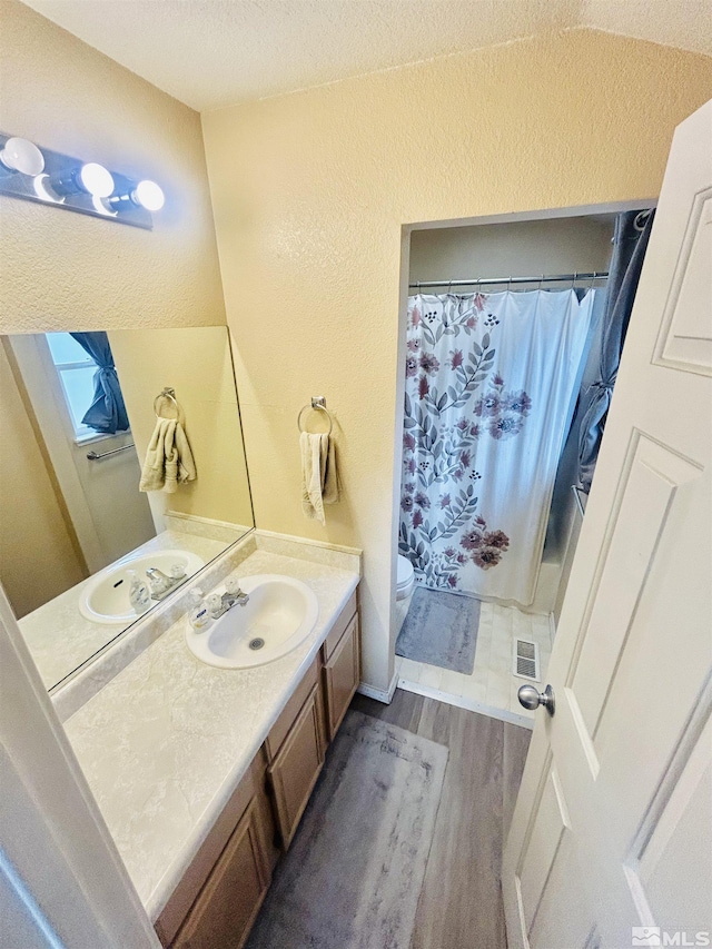 full bath with a textured ceiling, vanity, visible vents, wood finished floors, and a shower with shower curtain