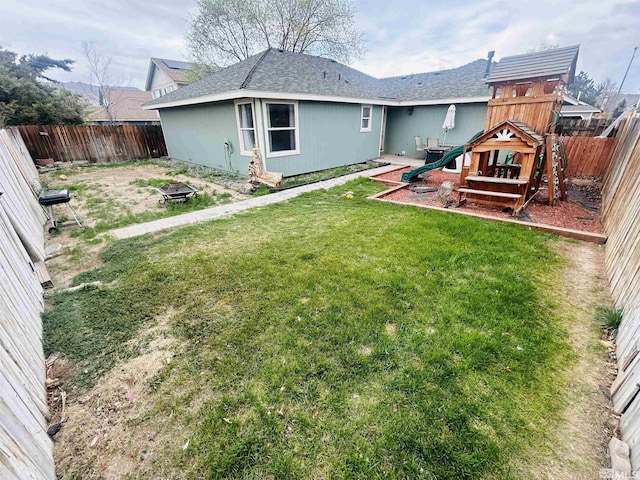 back of property with a yard, a fenced backyard, a playground, and roof with shingles