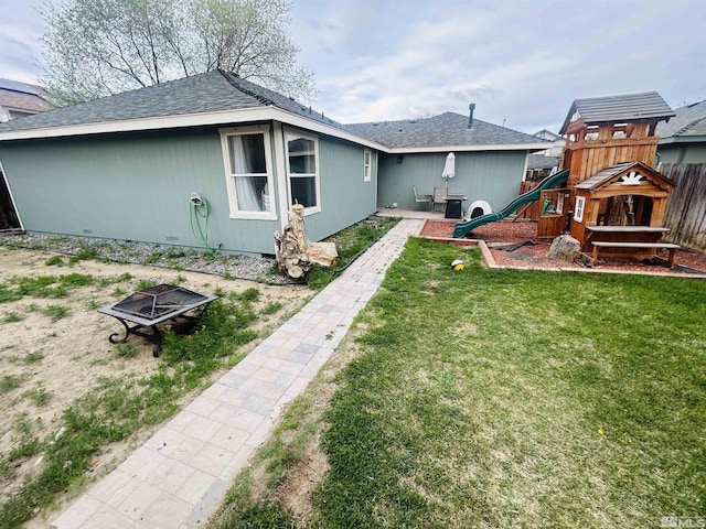 back of house with a yard, roof with shingles, and a playground
