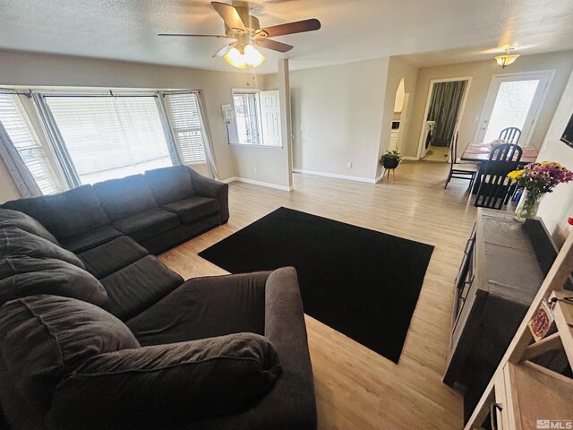 living room with ceiling fan, light wood finished floors, arched walkways, and baseboards