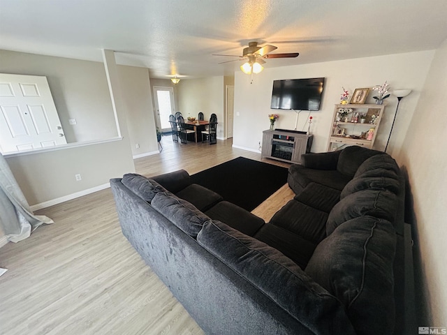 living area with a fireplace, ceiling fan, wood finished floors, and baseboards