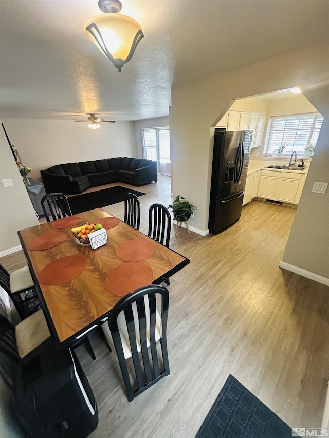 dining space with light wood finished floors, baseboards, a textured ceiling, and ceiling fan