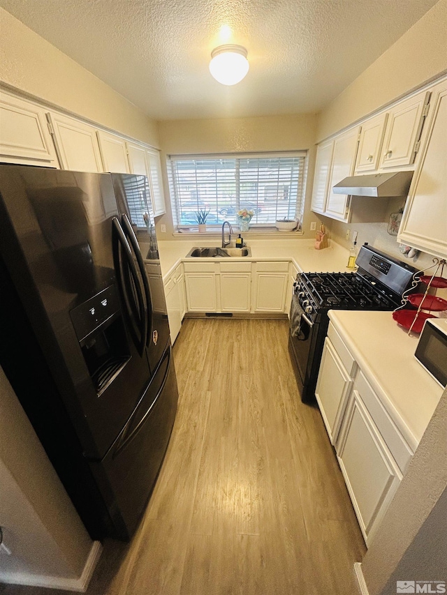 kitchen featuring black fridge with ice dispenser, gas range, under cabinet range hood, light wood finished floors, and a sink