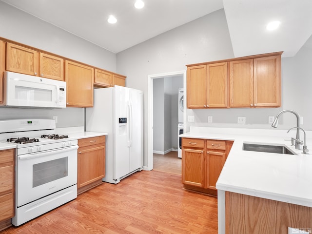 kitchen featuring a sink, light countertops, white appliances, stacked washer and dryer, and light wood finished floors