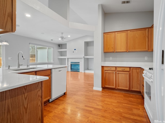 kitchen featuring a sink, ceiling fan, light wood-type flooring, white appliances, and a glass covered fireplace
