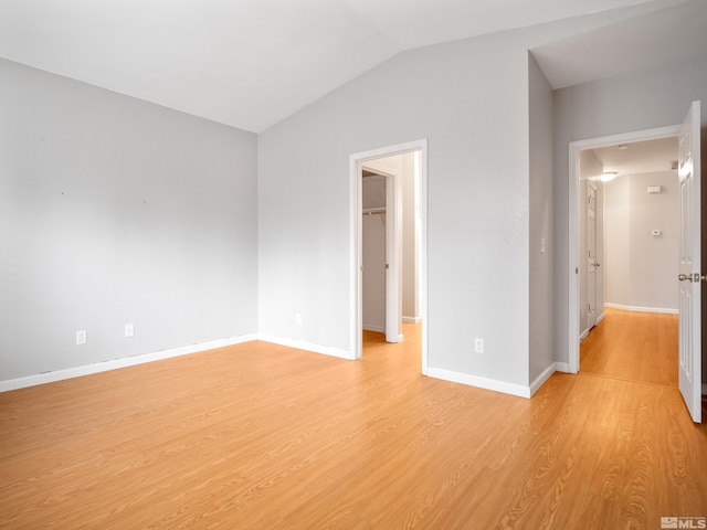 unfurnished bedroom featuring light wood-type flooring, baseboards, a spacious closet, and vaulted ceiling