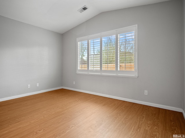 spare room with light wood finished floors, baseboards, vaulted ceiling, and visible vents