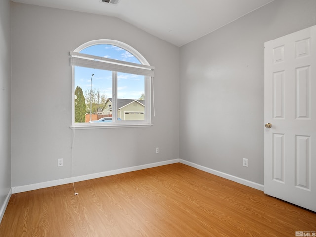 empty room with light wood-type flooring, visible vents, baseboards, and vaulted ceiling
