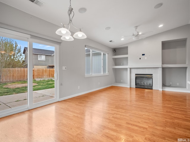 unfurnished living room with light wood-type flooring, built in shelves, a ceiling fan, visible vents, and a tile fireplace