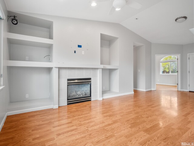 unfurnished living room featuring lofted ceiling, light wood-type flooring, built in features, ceiling fan, and a tile fireplace