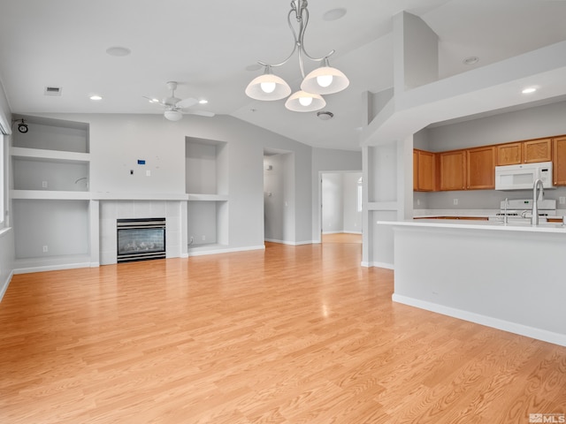unfurnished living room featuring a ceiling fan, light wood-style floors, built in features, a tiled fireplace, and lofted ceiling