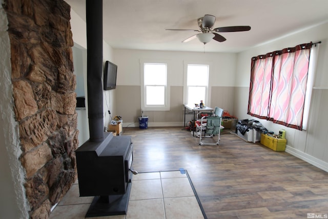 living area featuring wood finished floors, a wood stove, baseboards, and a ceiling fan