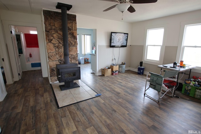 living room with wood finished floors, a wood stove, and a ceiling fan
