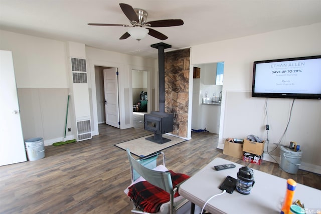 living room featuring a wood stove, a ceiling fan, and wood finished floors