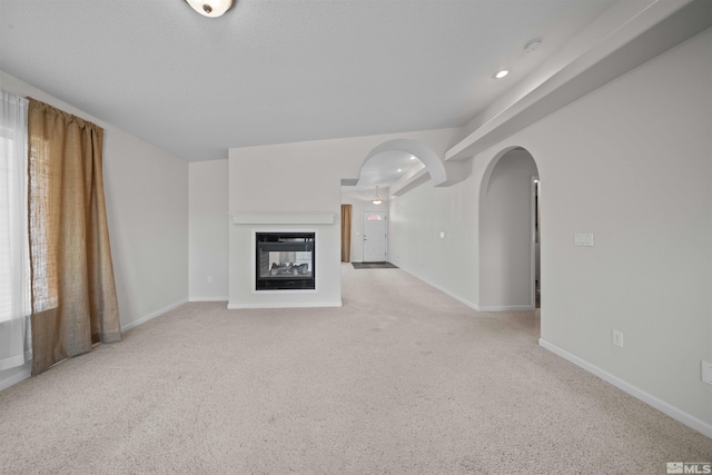 unfurnished living room featuring arched walkways, light carpet, and baseboards