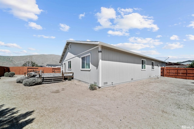 view of property exterior featuring a deck with mountain view, crawl space, and a fenced backyard