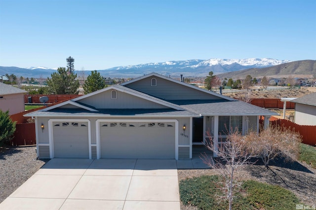 ranch-style house featuring fence, concrete driveway, an attached garage, roof with shingles, and a mountain view