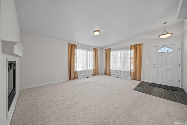 carpeted entrance foyer featuring a glass covered fireplace, vaulted ceiling, visible vents, and baseboards