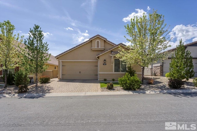 ranch-style home featuring an attached garage, fence, decorative driveway, and stucco siding