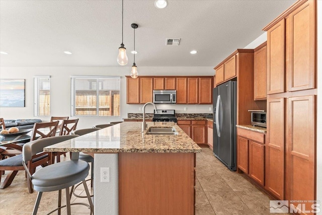 kitchen with a kitchen breakfast bar, light stone counters, stainless steel appliances, visible vents, and a sink
