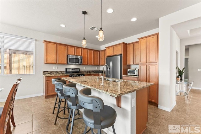 kitchen featuring brown cabinetry, appliances with stainless steel finishes, light stone counters, and a sink