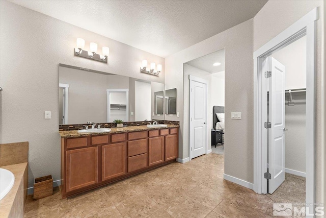 bathroom with a walk in closet, a relaxing tiled tub, a sink, and double vanity