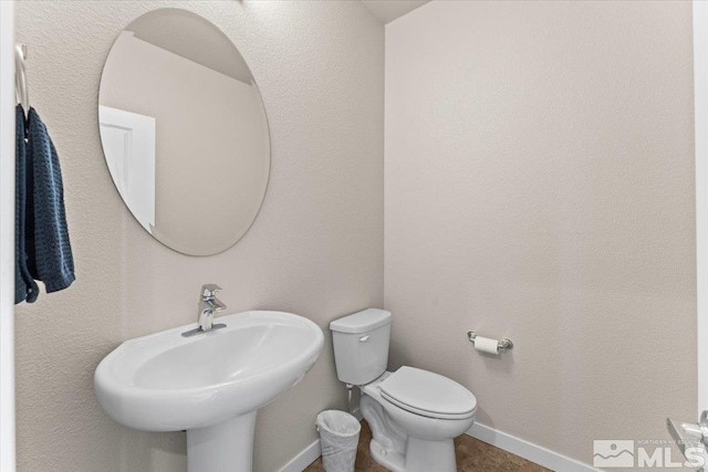 half bathroom featuring baseboards, a sink, and toilet