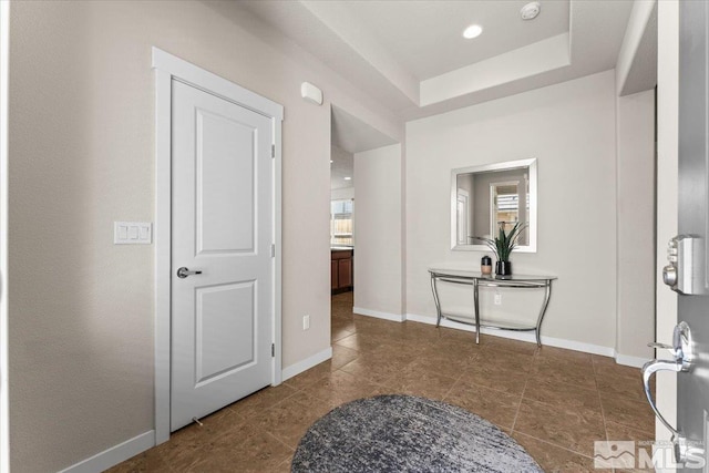tiled entryway with a tray ceiling and baseboards