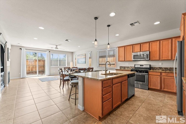 kitchen featuring brown cabinets, light stone counters, visible vents, a sink, and appliances with stainless steel finishes