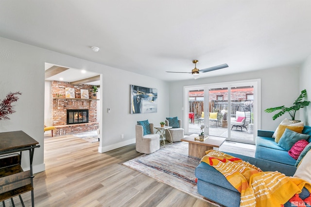living area featuring baseboards, a ceiling fan, a brick fireplace, and wood finished floors