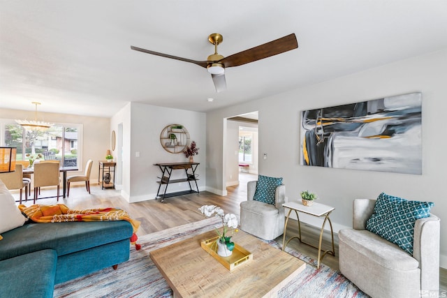 living room with wood finished floors, baseboards, and ceiling fan with notable chandelier