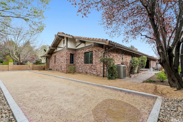 view of side of property featuring a tile roof, central AC, fence, brick siding, and stucco siding