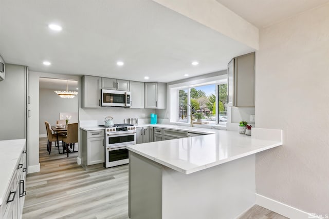 kitchen featuring gray cabinets, light wood-style floors, white microwave, range with two ovens, and a peninsula