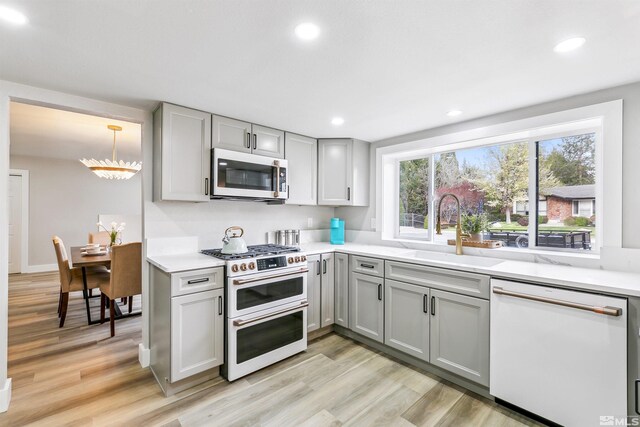 kitchen with a sink, stainless steel microwave, double oven range, white dishwasher, and gray cabinets
