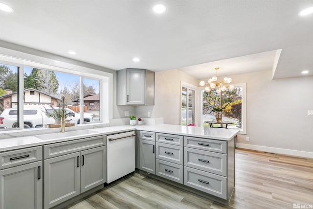 kitchen featuring a peninsula, white dishwasher, gray cabinetry, and light countertops