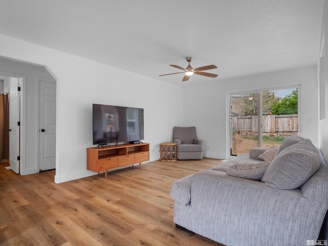living room with light wood-type flooring, a ceiling fan, baseboards, and arched walkways