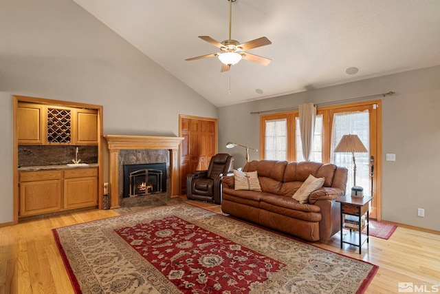living room featuring light wood finished floors, a ceiling fan, high vaulted ceiling, and a premium fireplace