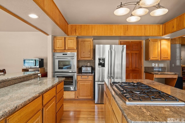 kitchen featuring stone countertops, a toaster, light wood-style floors, and appliances with stainless steel finishes