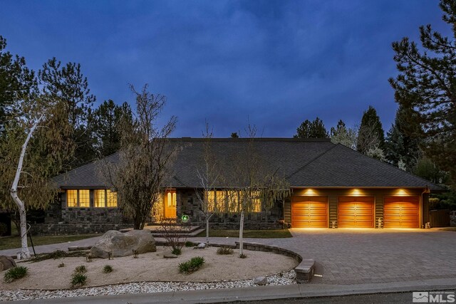 view of front of house with an attached garage, decorative driveway, stone siding, and a shingled roof