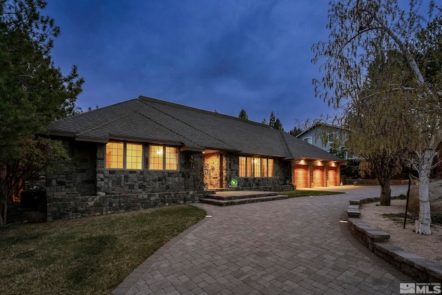 view of front facade featuring a shingled roof, a front lawn, curved driveway, an attached garage, and stone siding