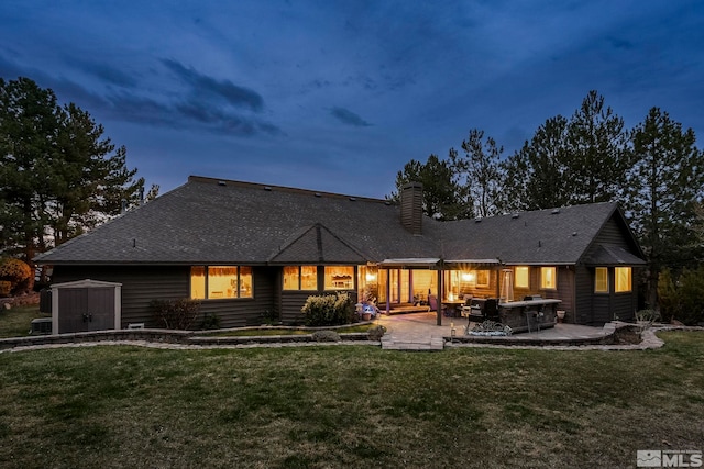 rear view of house featuring a chimney, a lawn, an outdoor structure, a shed, and a patio